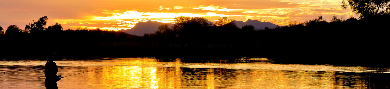 An angler on the edge of an Arizona lake is silhouetted by a bright orange sunset