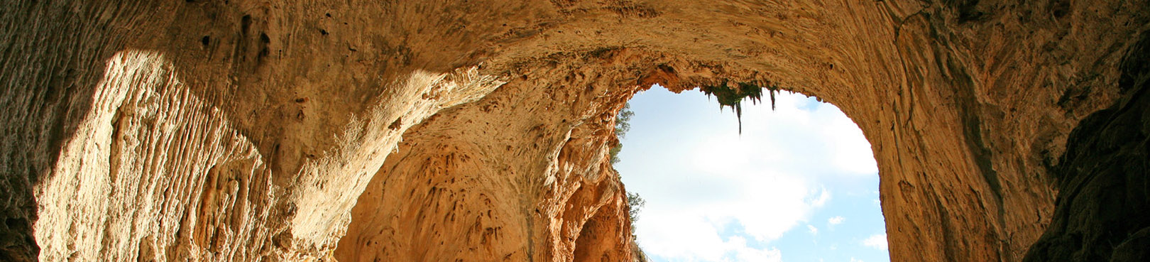 Looking through the natural bridge from beneath a ceiling of travertine south to partly cloudy skies.