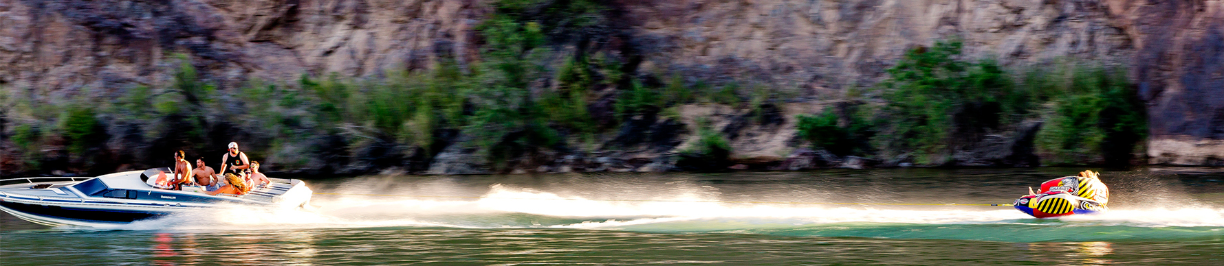 Water sprays as a speedboat pulls someone on a tube in the green water of the Colorado River.