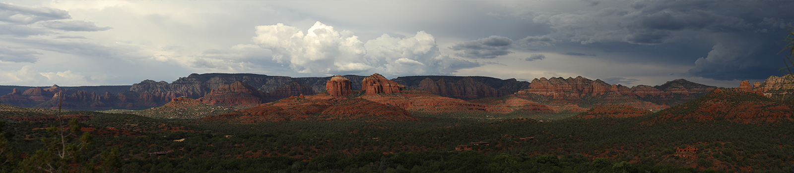 A panoramic view of the Sedona area showcases a contrast between the crimson colored rocks and a dark, dreary cloud filled sky.