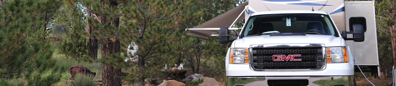 A truck and RV are backed into one of the popular forest campsites amid a sea of ponderosa pine trees.