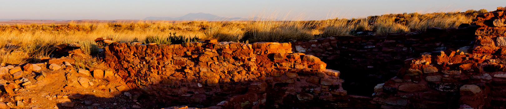 Ancient dwellings glow red in the late afternoon sun on the yellow Northern Arizona prairie.