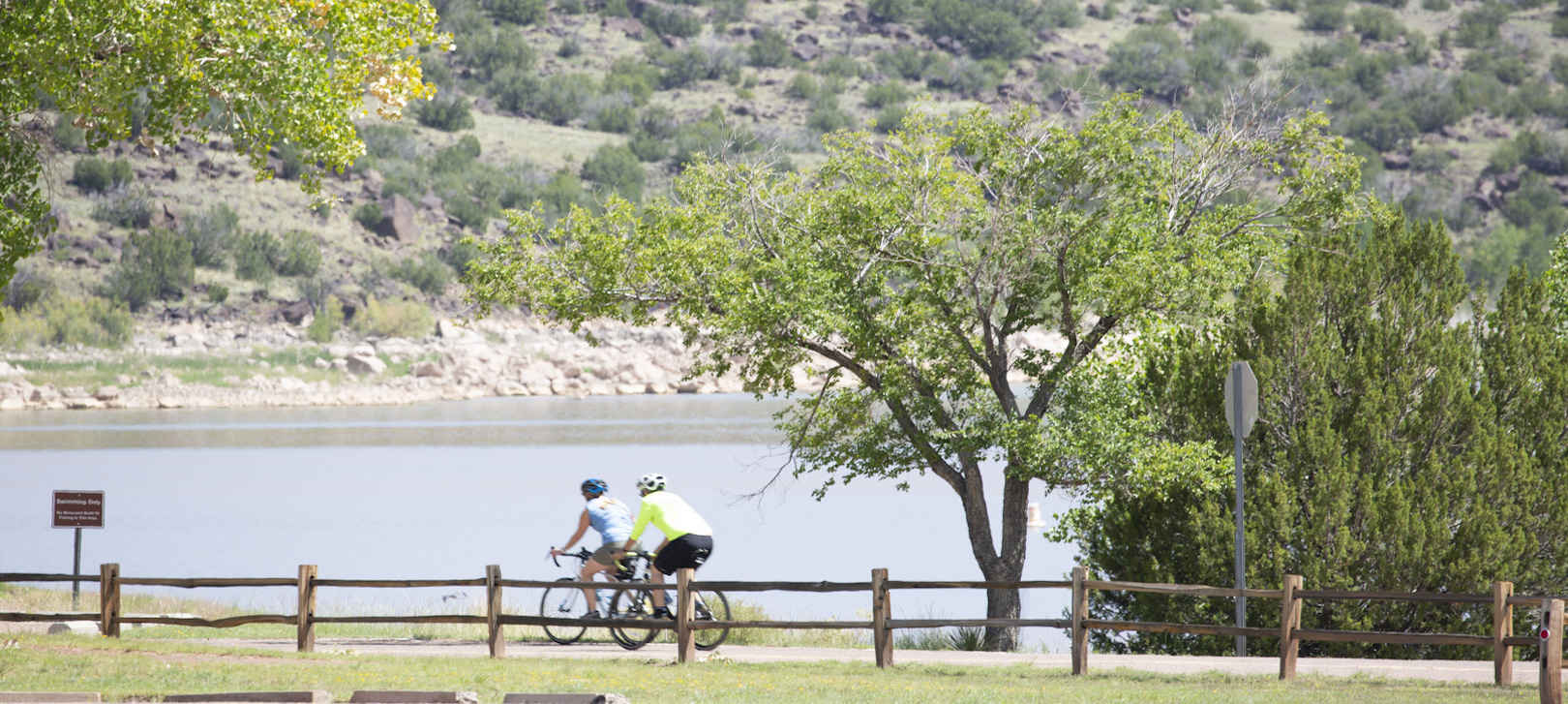 Two cyclists ride on a path along the lake