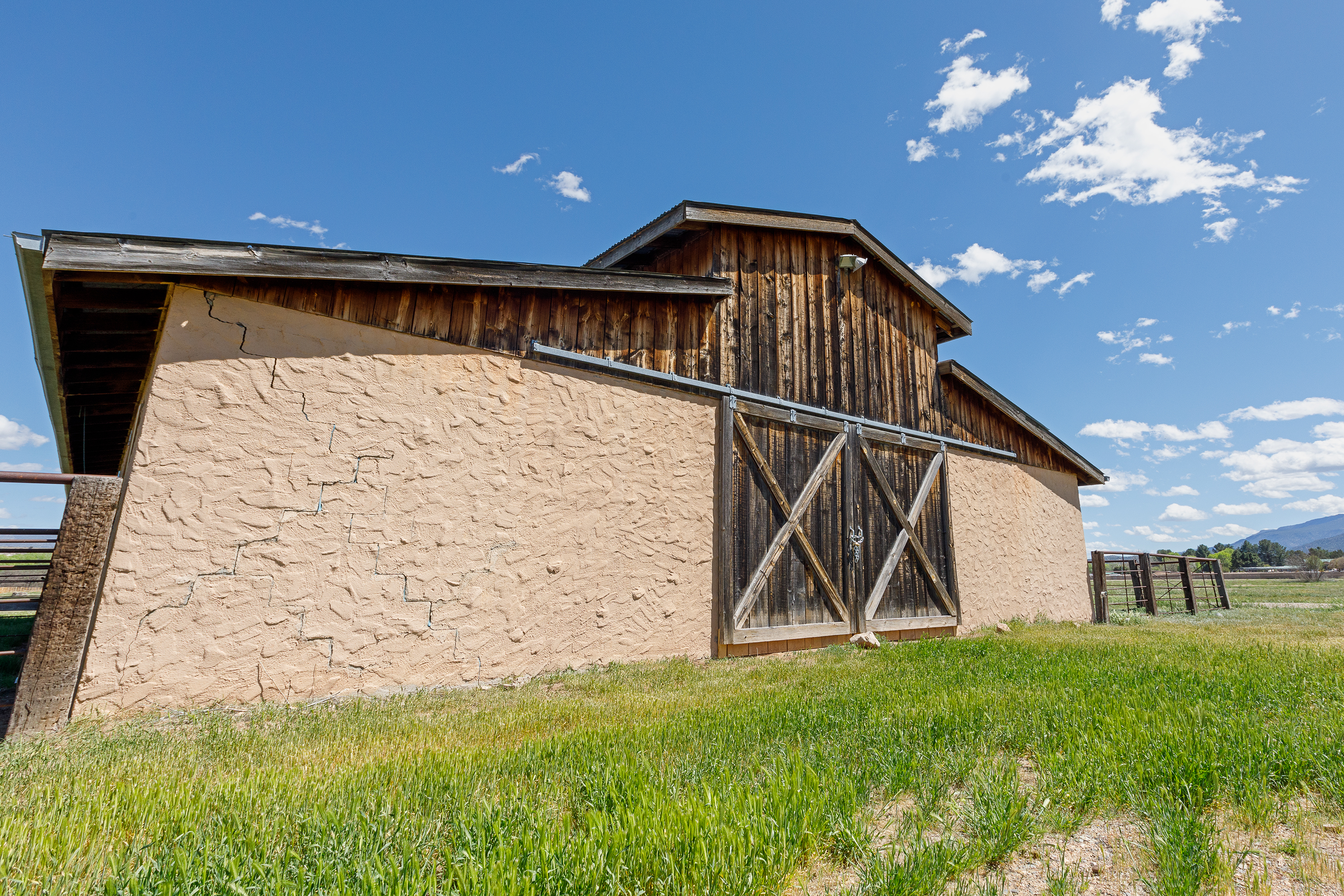 An old barn surrounded by green grass standing under a blue sky with puffy white clouds.