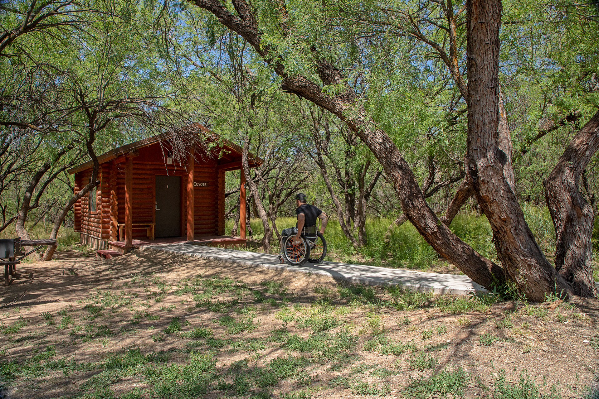 A man in a wheelchair heads to the door of a rental cabin in the trees at Dead Horse  Ranch State Park