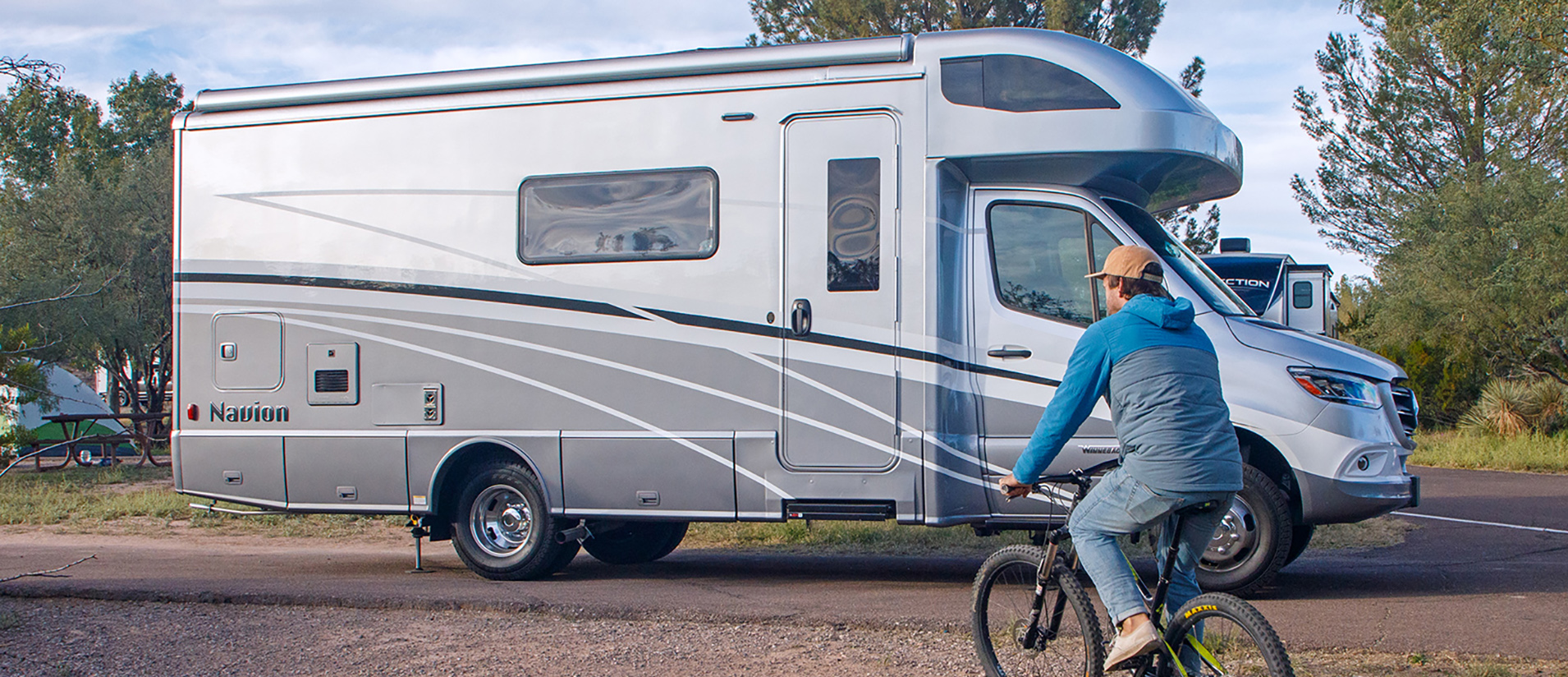 A man rides a bicycle past a gray RV camper at Dead Horse Ranch State Park