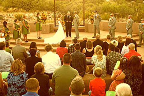 A wedding party standing on the raised platform at the front of an amphitheater. Wedding guests sit facing the wedding party.