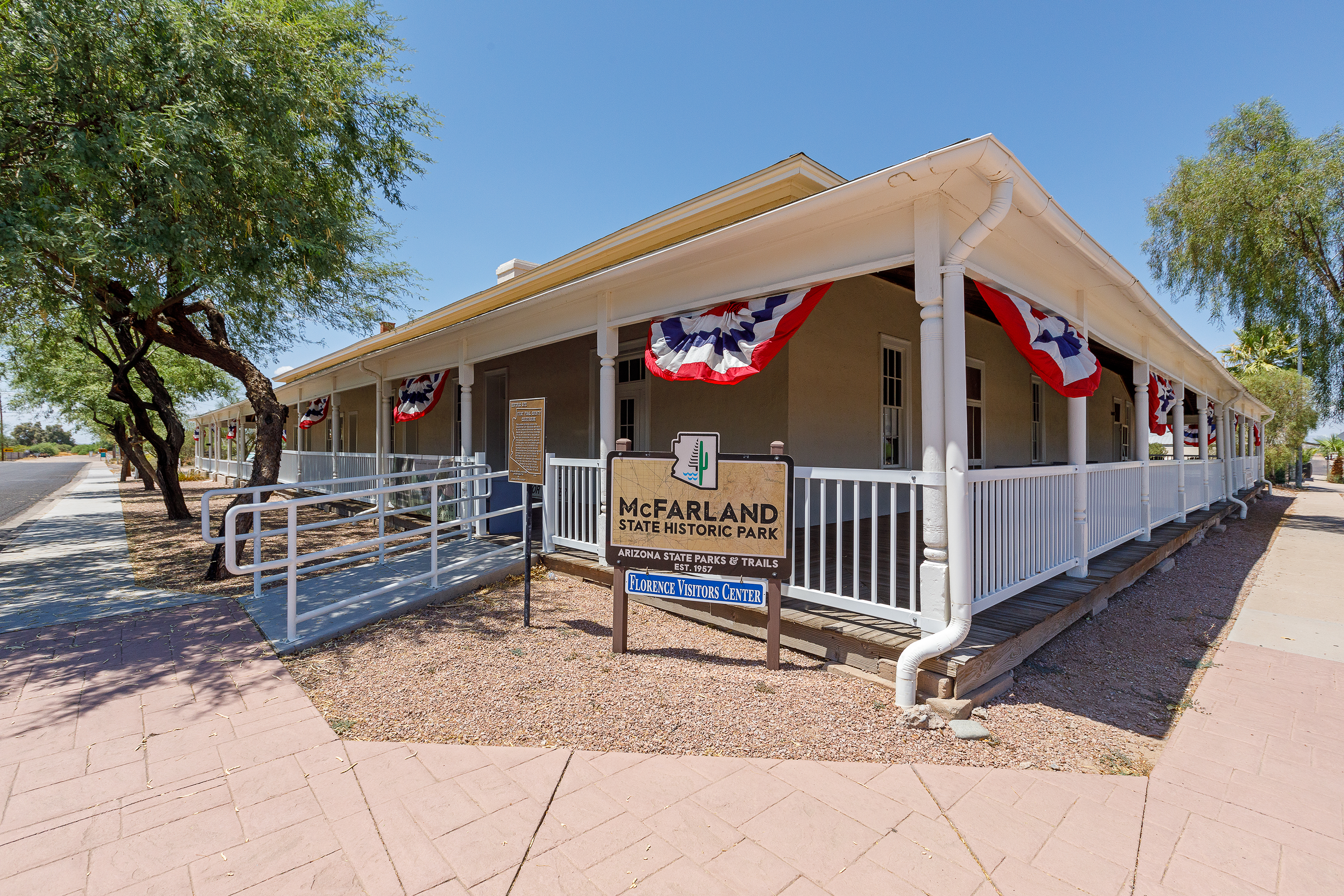 The entrance of McFarland State Historic Park with white railings and red, white and blue banners hanging from the ceilings of its wrap-around porch