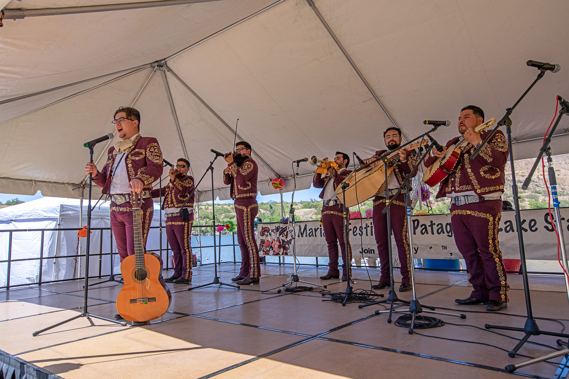 A mariachi band wearing maroon and gold suits sing and play their instruments on a stage.