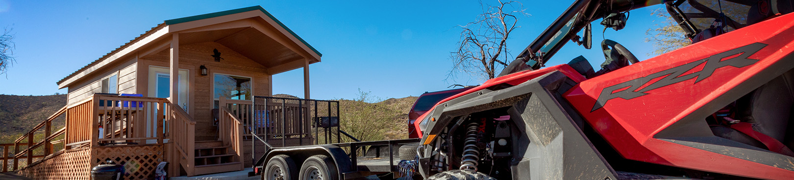 A Red off-highway vehicle (OHV) is parked just outside an Alamo Lake cabin and under a bluebird sky.