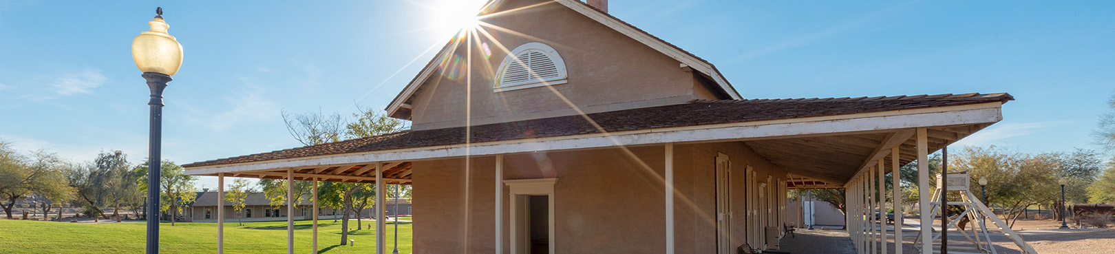 A Late morning sun peeks from behind the Quartermasters Depot to shine down on the bright green grass and  Victorian era light post.