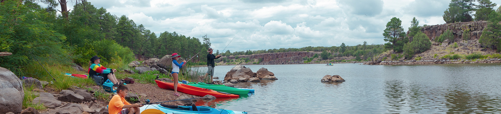 A group of kayakers takes a break on the rocky pine tree lined shore of Fool Hollow Lake.