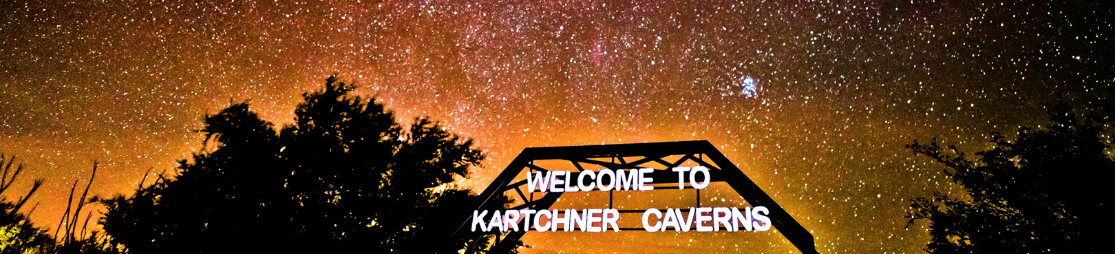 A layered image of the Milky Way glows orange above the Welcome to Kartchner Caverns sign.