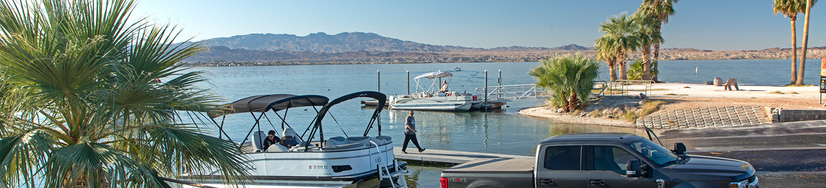 A truck launches a pontoon boat from one of the scenic Havasu boat ramps lined with palm trees.