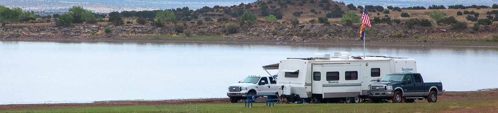 A large RV camper and two trucks at a scenic campsite on the shoreline just feet from the beautiful high-desert lake.