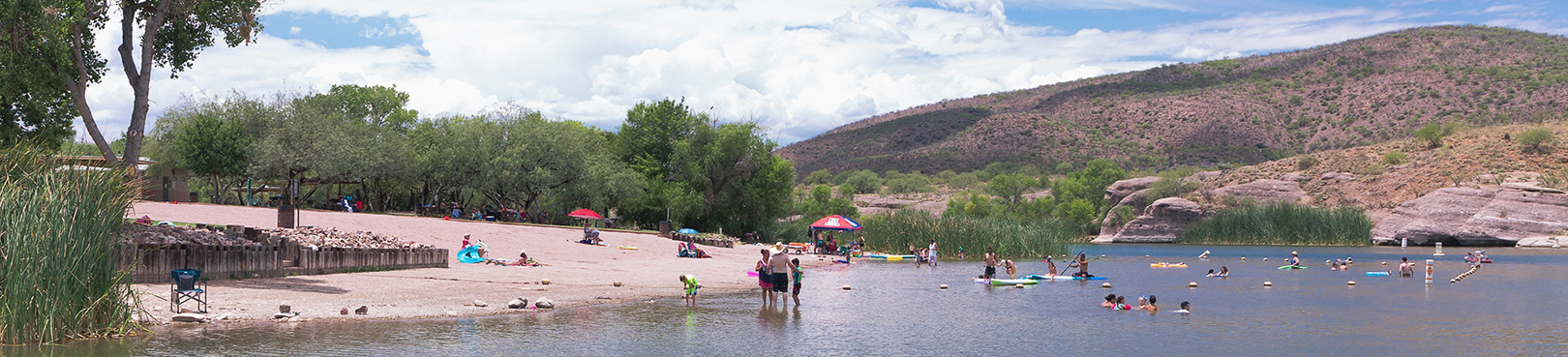 Visitors enjoying the Patagonia Lake beach area by lounging on the beach or while riding kayaks and paddle boards.