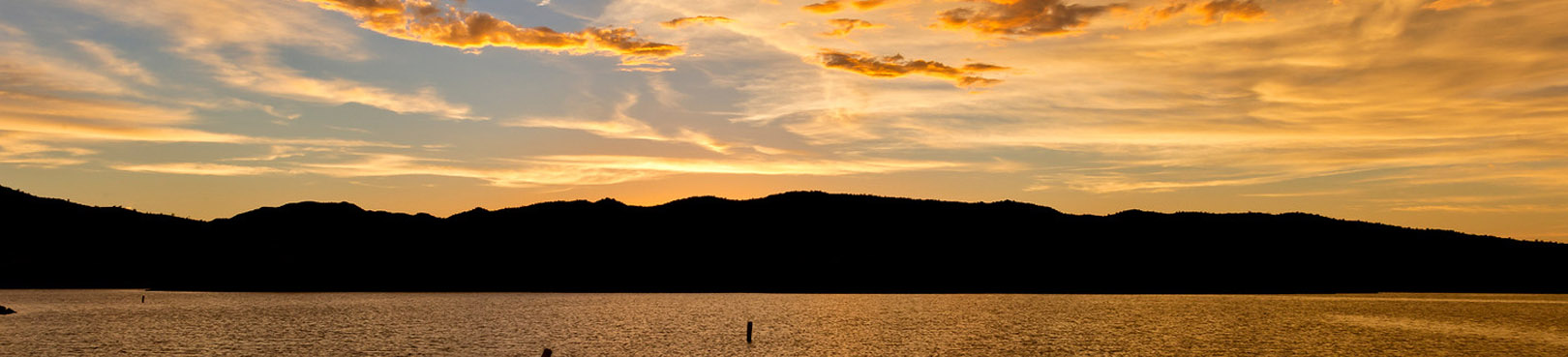 An orange Alamo Lake sunset illuminates the shimmering lake surface in front of silhouetted mountains in the distance.