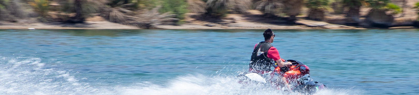 A person wearing a life jacket while riding a wave runner on blue water.