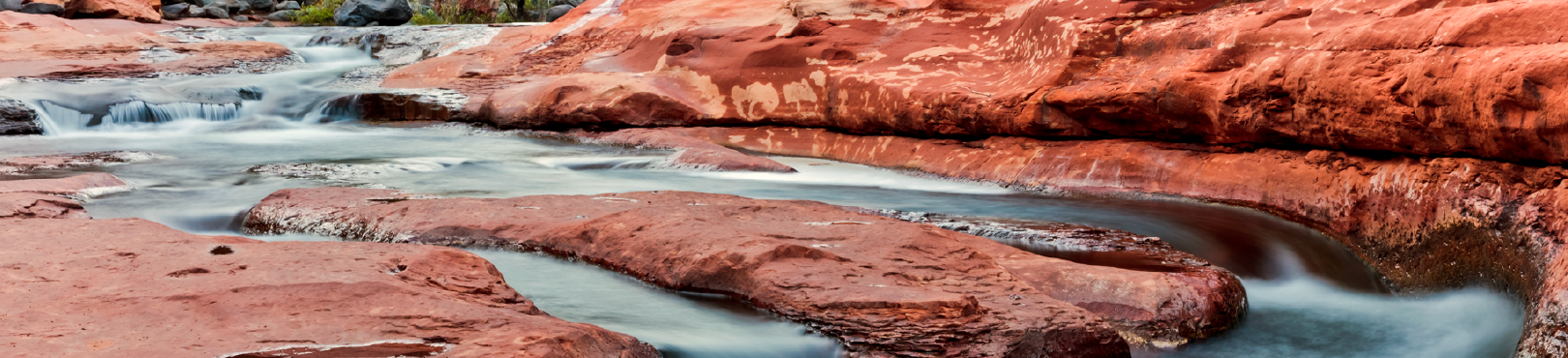 The clean waters of Oak Creek flowing through a creek bed of red rock.