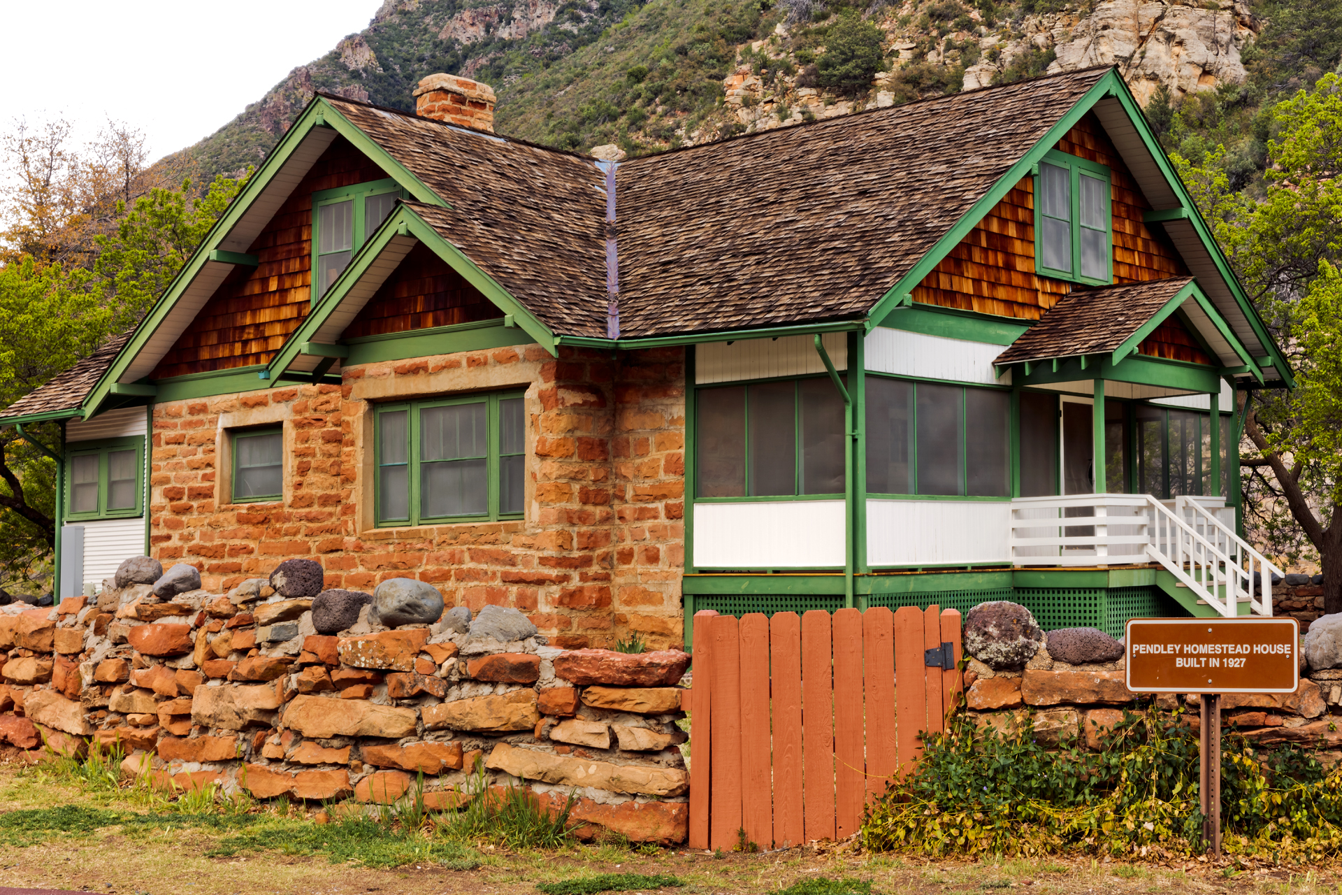 The historic 1927 Pendley homestead house with green trim, a white porch, brown sandstone siding, and wood shingles on the roof.