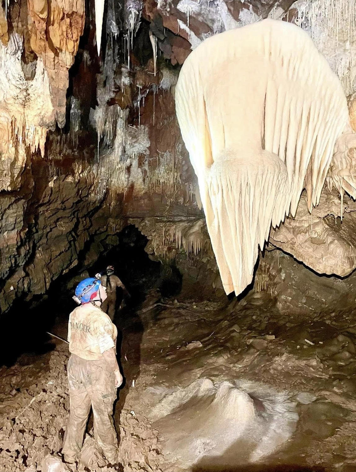 Chelsea Ballard, Cave Unit Manager at Kartchner Caverns, stands next to a large bright white flowstone formation that resembles an angel wing.