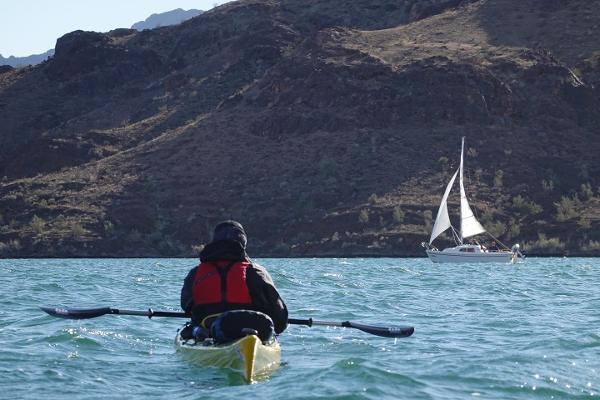 A kayaker on the water with a sailboat in the distance at Lake Havasu State Park