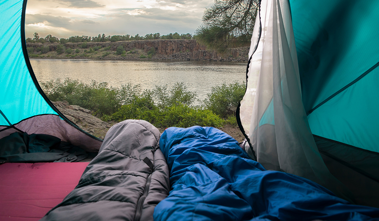 Camping checklist- Two people in sleeping bags looking out the door of their tent at Fool Hollow Lake.