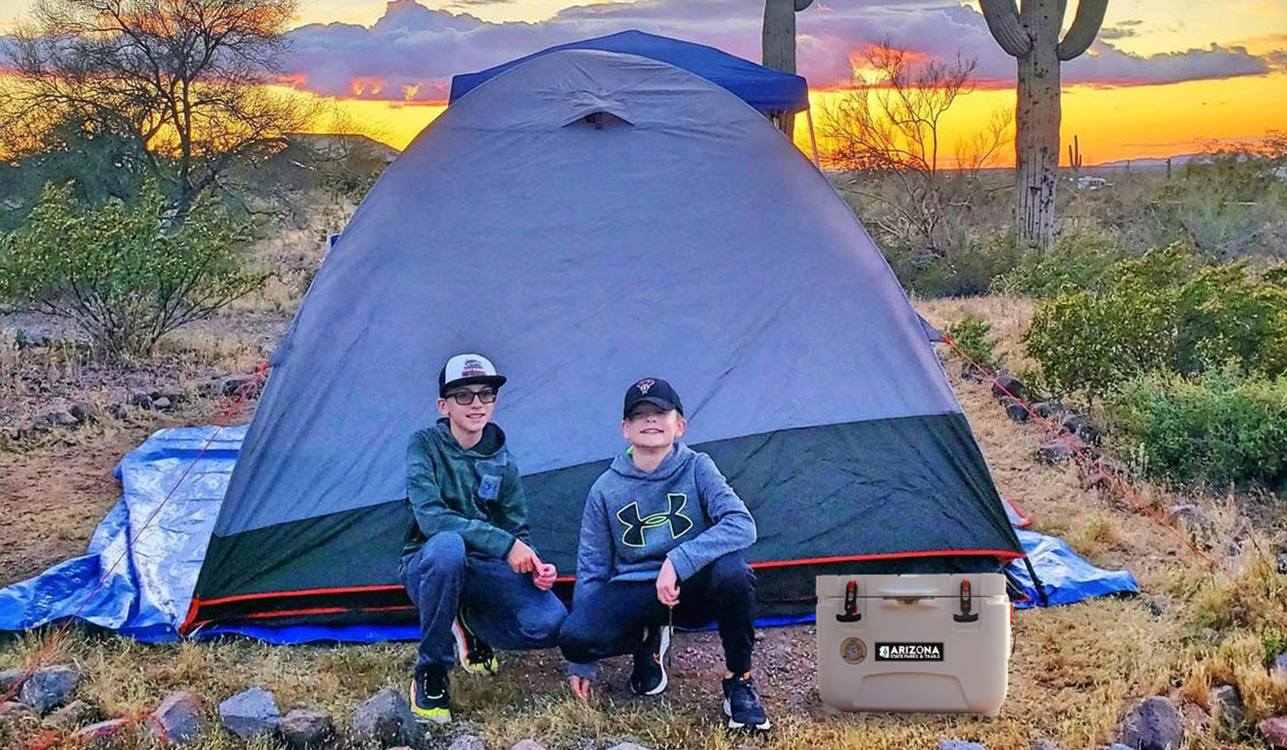 Camping checklist- Kids posing at a desert campsite next to a roto molded cooler.