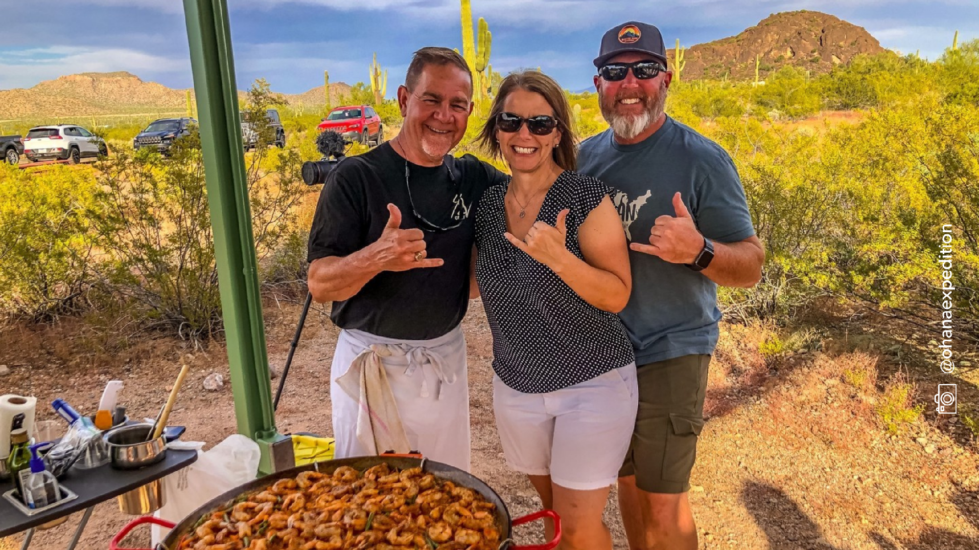 Photo of three adults standing around a dish of food prepared at the campground