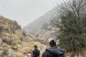 Hikers making their way through light snowfall in desert scrub and grassland at the base of the Whetstone Mountains in Kartchner Caverns State Park.