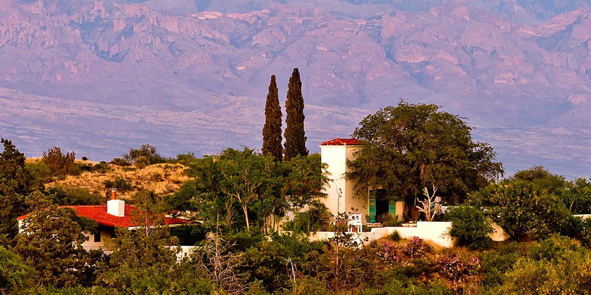 A closer view of the Kannally Ranch House with its red tile shingle roof, white adobe, and turquoise shutters.