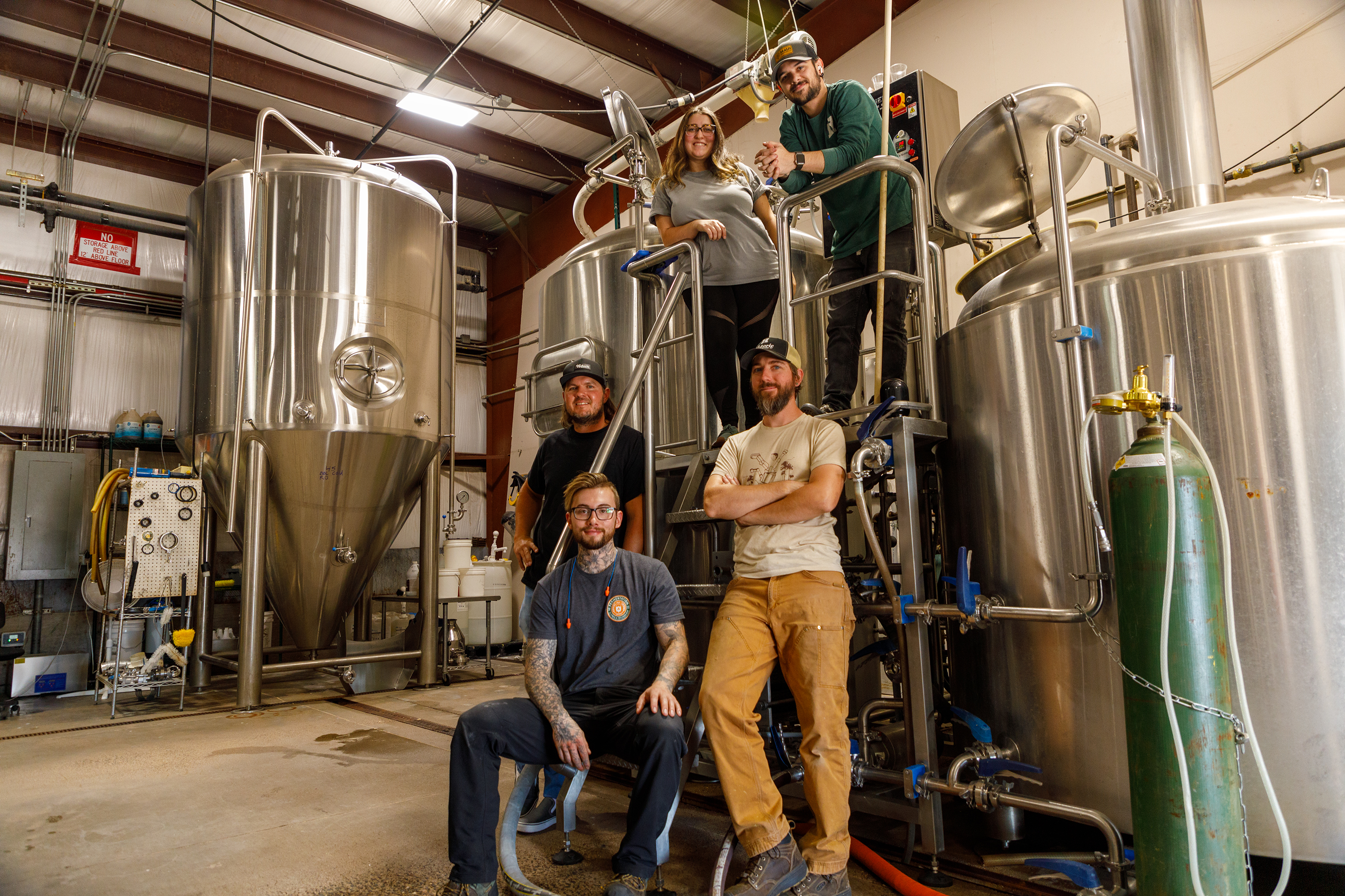 Five members of the Historic Brewing Company team poses in front of large metal brewing tanks and equipment.