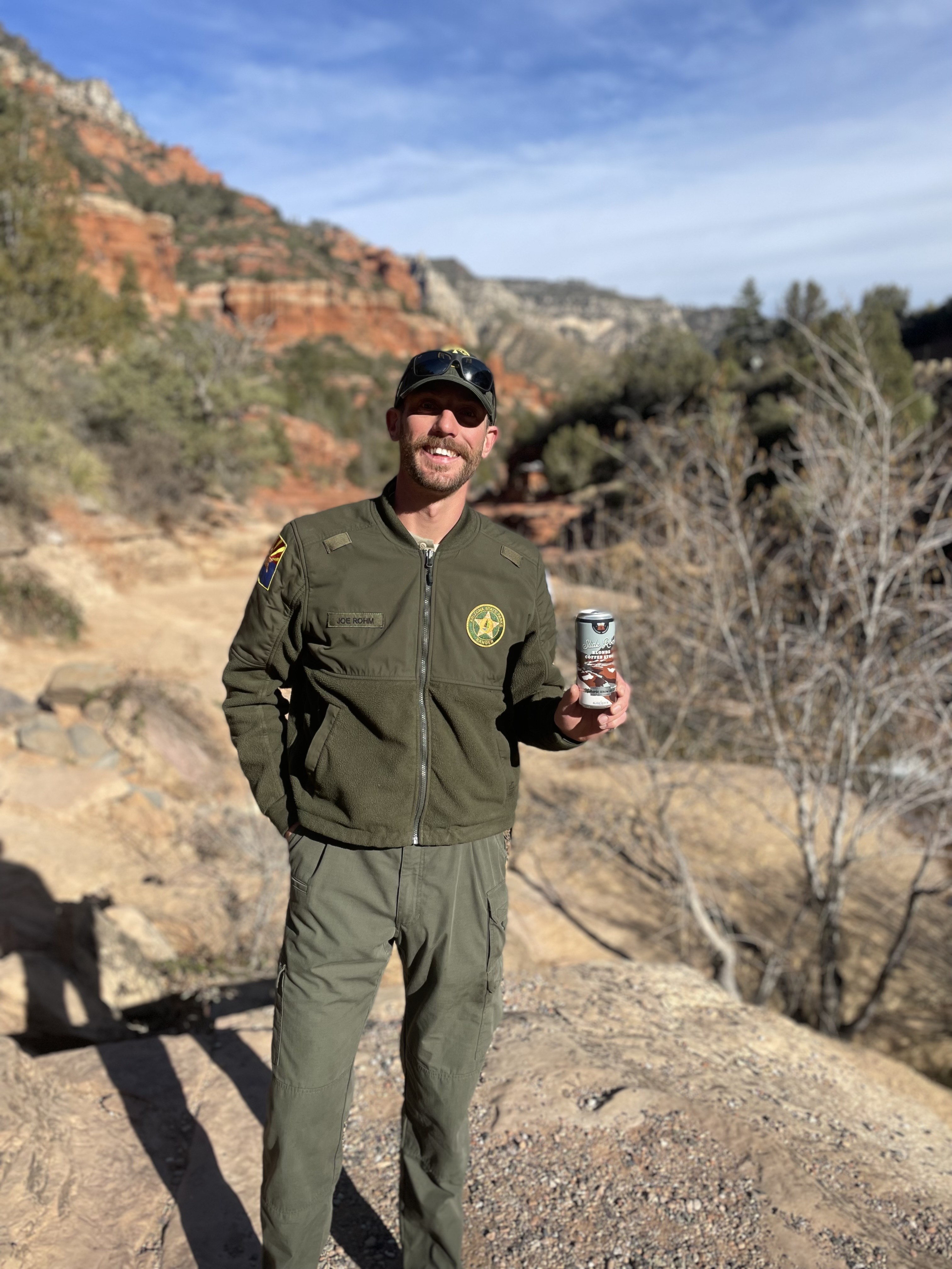 A park ranger stands on an overlook at Slide Rock, with Oak Creek below. He holds a can of the new Blonde Coffee Stout in his hand.