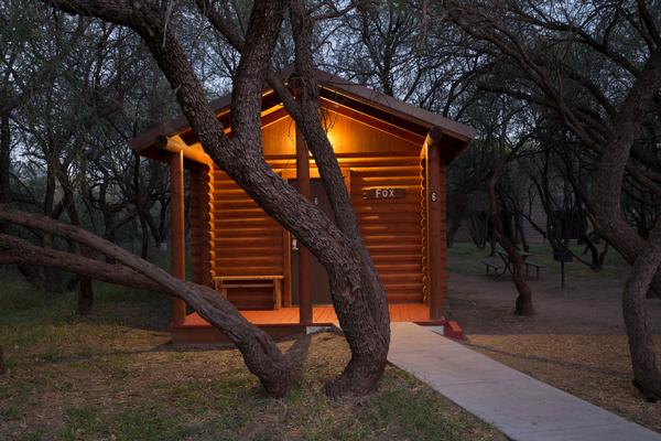 A cabin at Dead Horse Ranch State Park with shade trees and a warm glow.