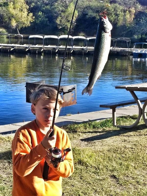 Child displaying a nice Rainbow trout wih Patagonia Lake in the background. Patagonia is stocked with trout throughout the winter.   