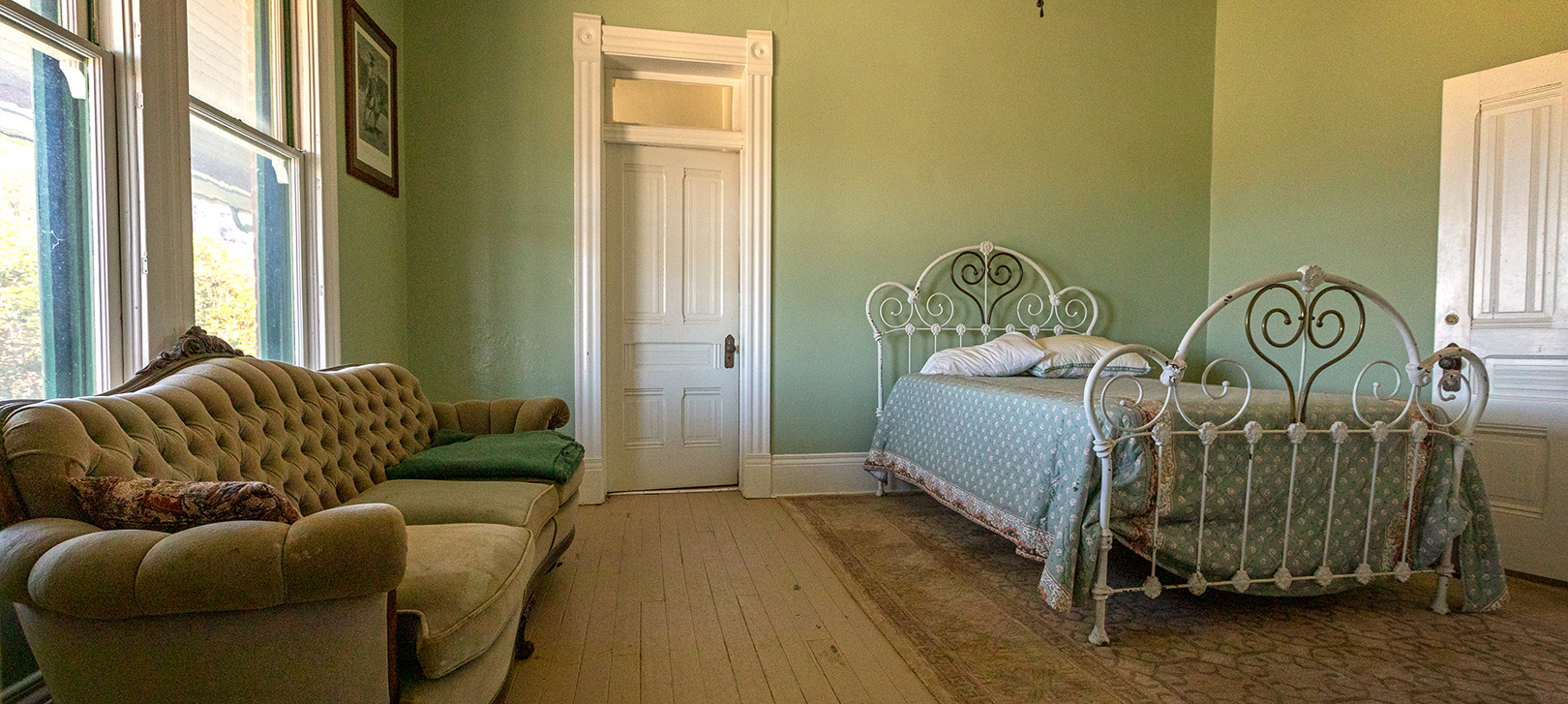 A sofa and bed with old-fashioned head and footboards inside a green room at the San Rafael Ranch House