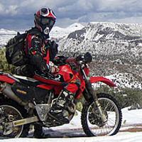 A dirtbiker poses with his bike in a snow covered high desert setting.