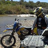 A man on a dirt bike takes a break at the edge of a desert creek.